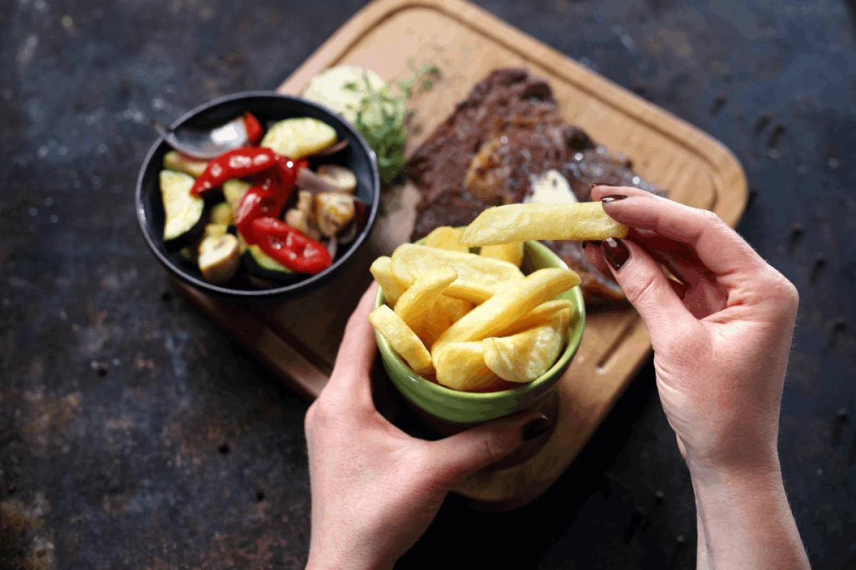 Domowe frytki w zielonej misce, w tle upieczone mięso z sałatką